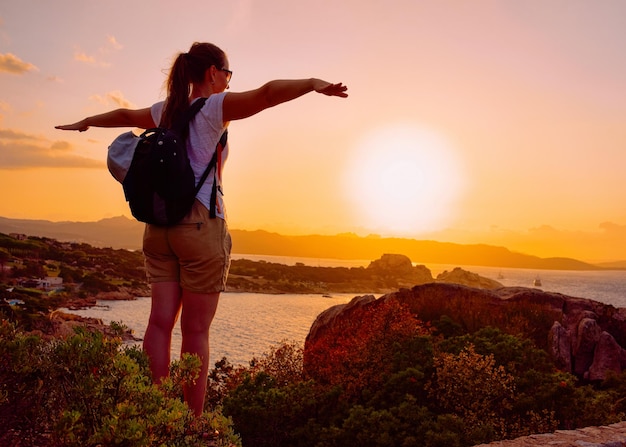 Sunrise or sunset and young lady at Baja Sardinia in Costa Smeralda at Mediterranean sea in Sardinia island in Italy. Boat in Sardegna in summer.