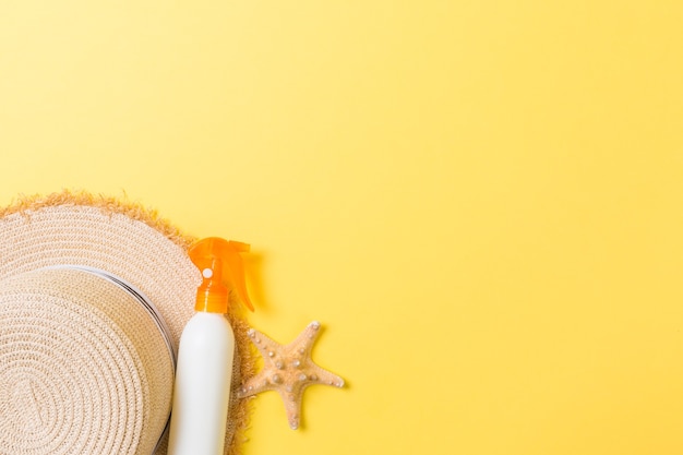 Sunscreen bottles with starfish and sunhat on yellow table with copy space. Travel healthcare accessories top view.