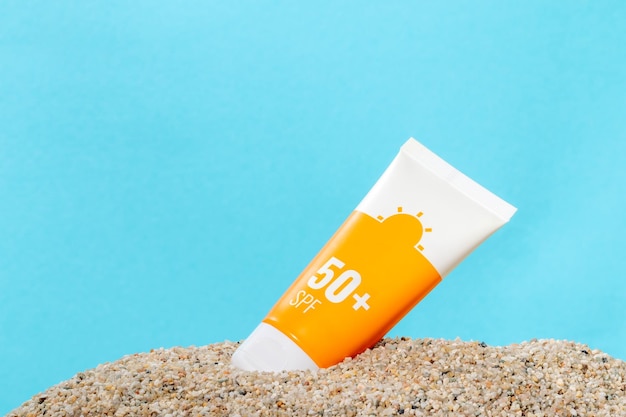 Sunscreen in an orange tube on blue background with beach sand copy space Summer beach vacation concept spf uvprotect cosmetics