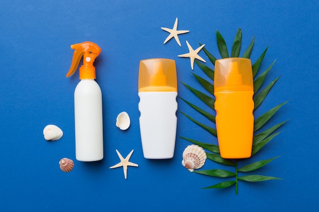 Sunscreen spray bottle Bottle with sun protection cream and sea shells with tropical green leaf on color background top view