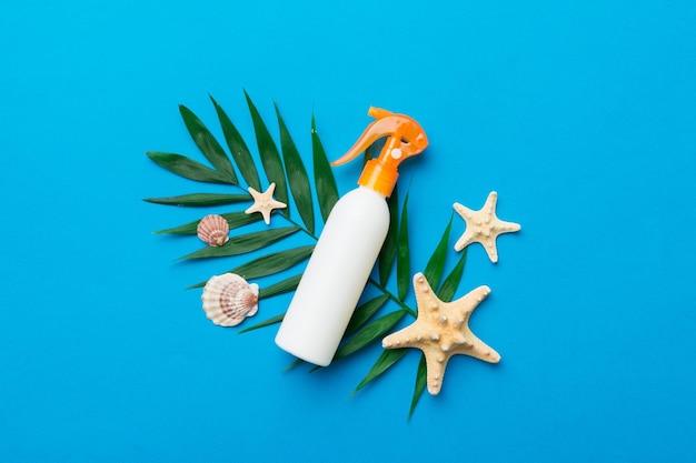 Sunscreen spray bottle Bottle with sun protection cream and sea shells with tropical green leaf on color background top view