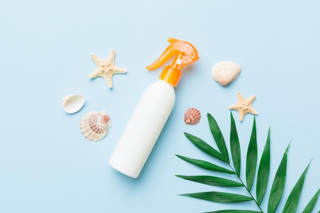 Sunscreen spray bottle Bottle with sun protection cream and sea shells with tropical green leaf on color background top view