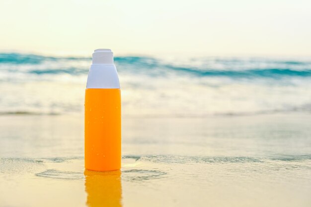 Sunscreen spray in orange bottle on the sand against the backdrop of sea waves