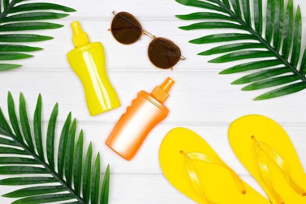 Sunscreen suntan products sunglasses flip flop sandals with tropical palm leaves Summer vibes