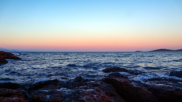 A sunset on the beach with a rock in the foreground and a small island in the background.