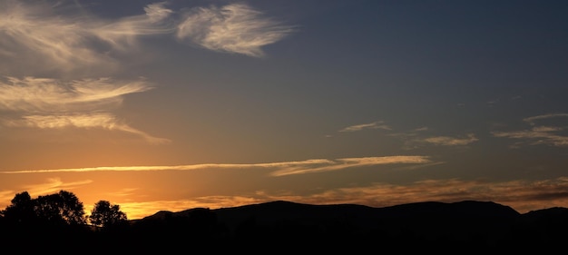 Sunset over hills silhouette scattered clouds on the sky The sundown is on the left side