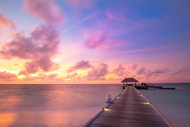 Sunset on Maldives island, luxury resort, wooden pier beautiful colorful sky and clouds and beach