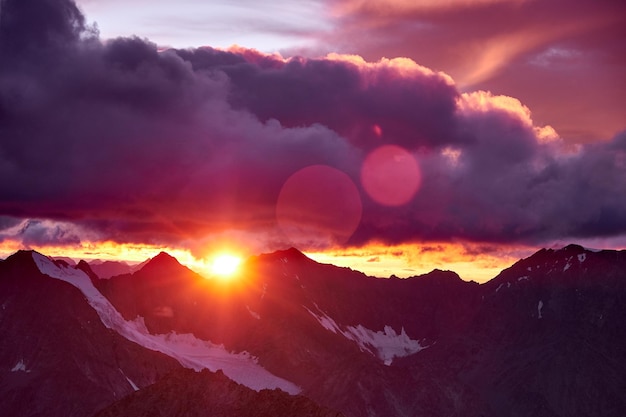 Sunset in mountains. Reflection of red sun on mountain snow peaks and clouds. Altai, Belukha area.