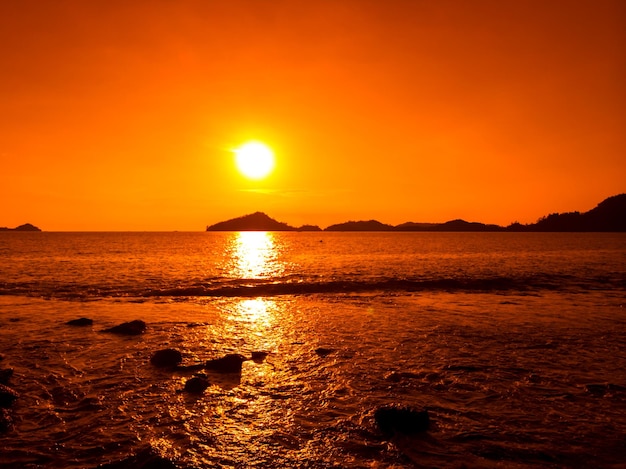 A sunset over the ocean with a large orange sky and the sun setting over the ocean.