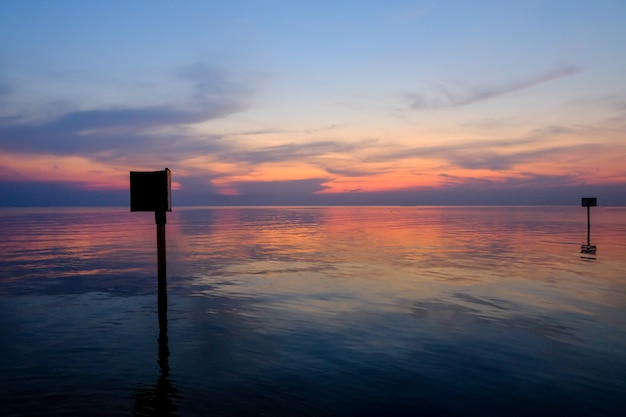 Sunset scene with warning marking steel pole in the sea, twilight time.