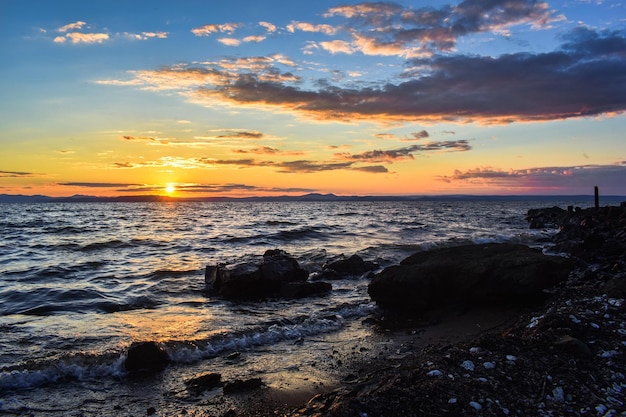 Sunset on the sea, on which the waves threw a lot of algae and shells. Sunlight is reflected in the