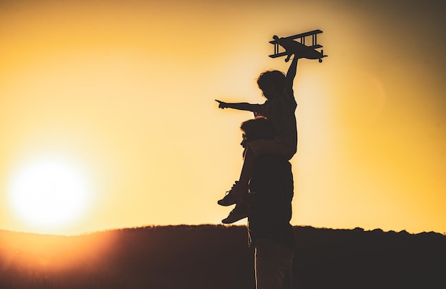 Sunset silhouette of child and dad playing kid pilot aviator and daddy dreams of traveling happy boy...