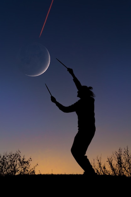 Sunset silhouette of a man with drumsticks,  Interaction with moon