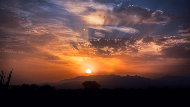 Sunset with rays between the clouds and horizon in the background. Colres brown, orange and blue.