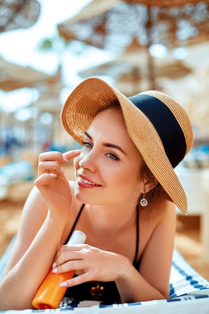 Suntan woman in hat applying sunscreen solar Beautiful happy woman smear lotion