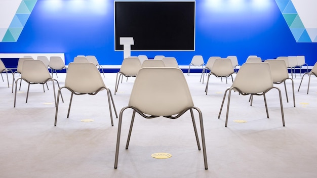 Super conference hall with white chairs and colored illumination and blank screen social distance