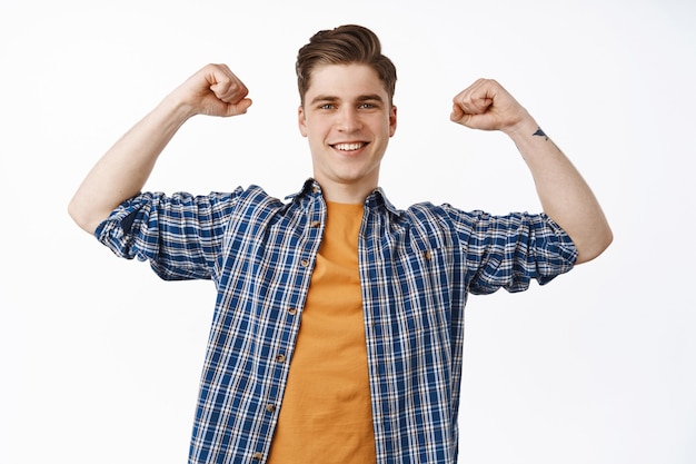 Super happy young man chanting, celebrating victory, raising hands in fist pumps and smiling pleased, winning and triumphing, standing on white