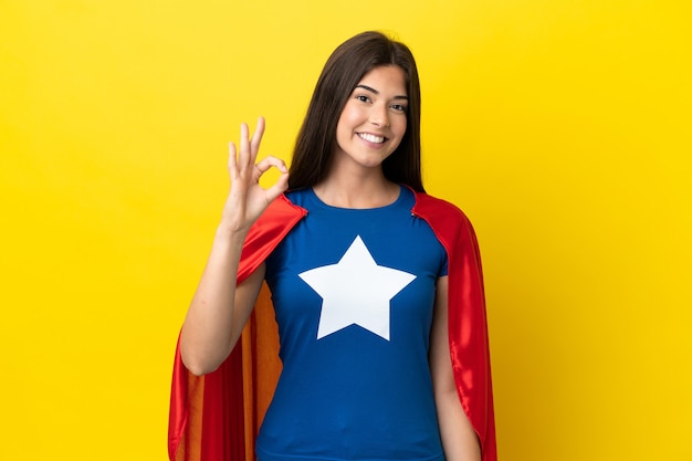 Super Hero Brazilian woman isolated on yellow background showing ok sign with fingers