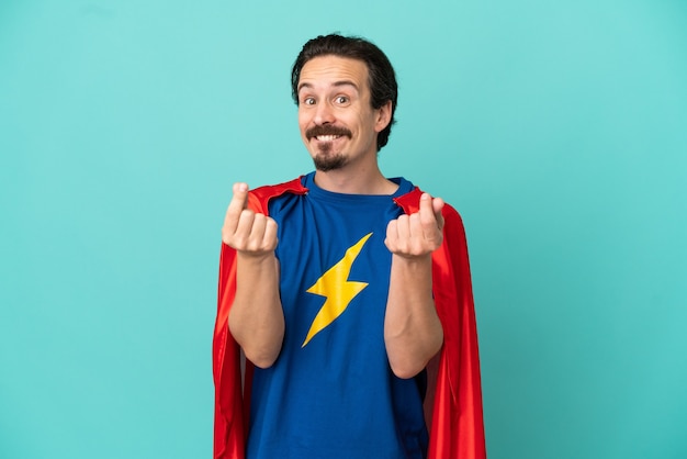 Super Hero caucasian man isolated on blue background making money gesture