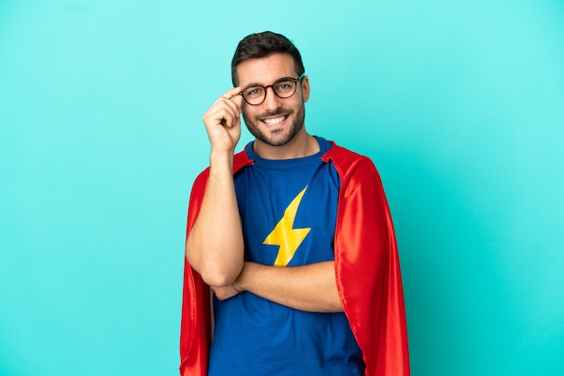 Photo super hero caucasian man isolated on blue background with glasses and happy