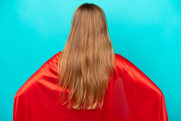 Super Hero caucasian woman isolated on blue background in back position