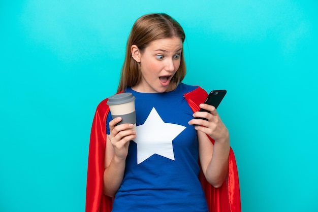 Super Hero caucasian woman isolated on blue background holding coffee to take away and a mobile