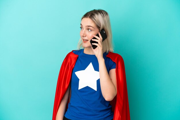 Super Hero caucasian woman isolated on blue background keeping a conversation with the mobile phone with someone