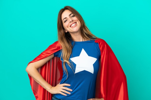 Super Hero caucasian woman isolated on blue background posing with arms at hip and smiling