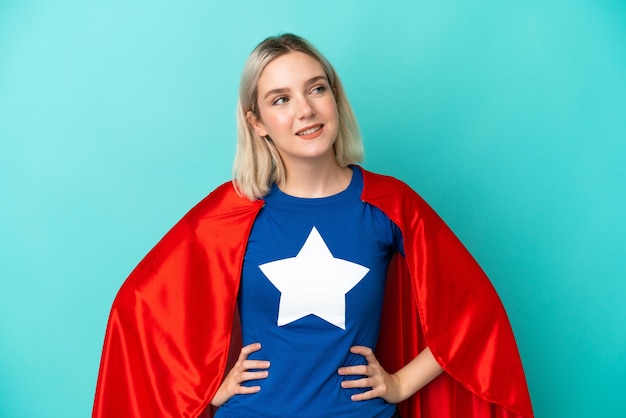 Super Hero caucasian woman isolated on blue background posing with arms at hip and smiling