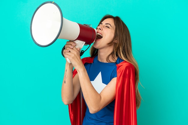 Super Hero caucasian woman isolated on blue background shouting through a megaphone