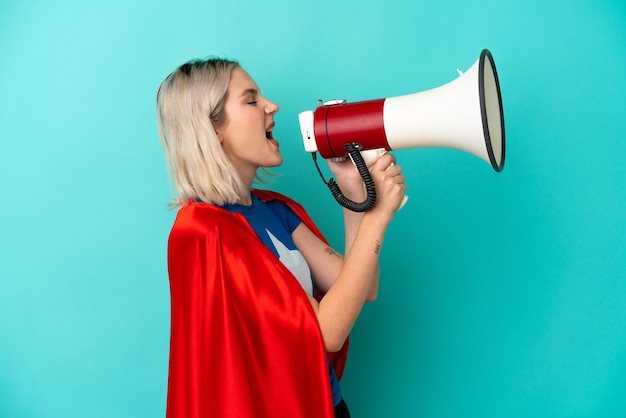 Super Hero caucasian woman isolated on blue background shouting through a megaphone