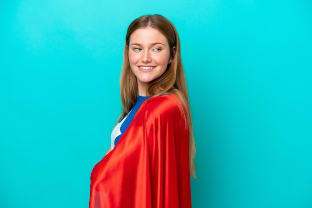 Super Hero caucasian woman isolated on blue background with arms crossed and happy