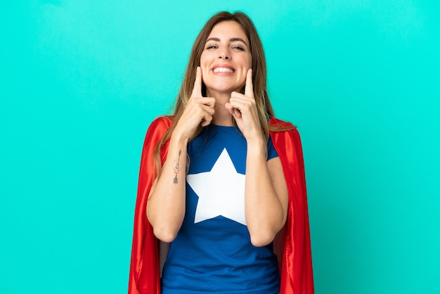 Super Hero caucasian woman isolated on blue wall smiling with a happy and pleasant expression