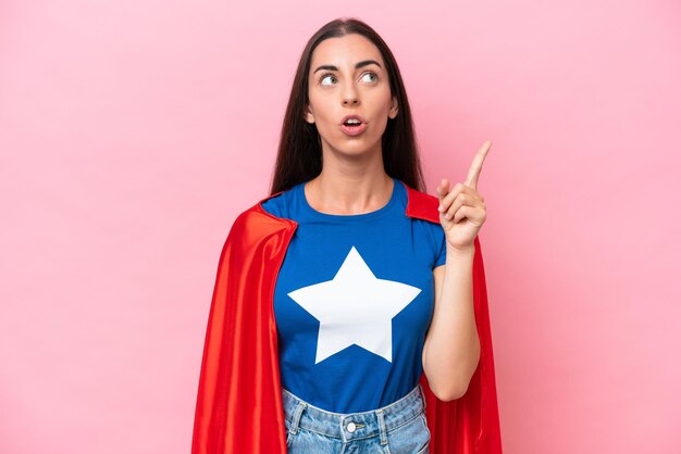 Super Hero Caucasian woman isolated on pink background thinking an idea pointing the finger up