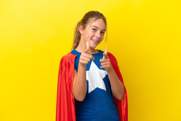 Super Hero little girl isolated on yellow background pointing to the front and smiling