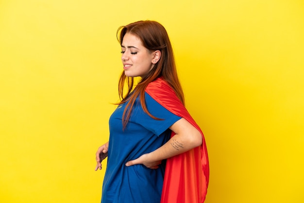 Super Hero redhead woman isolated on yellow background suffering from backache for having made an effort