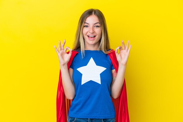 Super Hero Romanian woman isolated on yellow background showing an ok sign with fingers