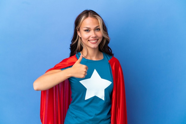 Super Hero Teenager girl isolated on blue background giving a thumbs up gesture