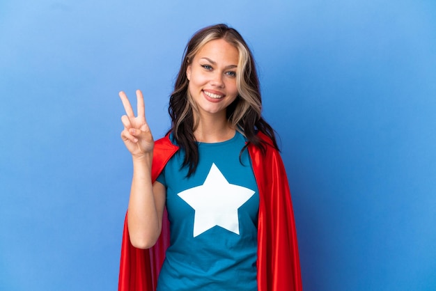 Super Hero Teenager girl isolated on blue background smiling and showing victory sign