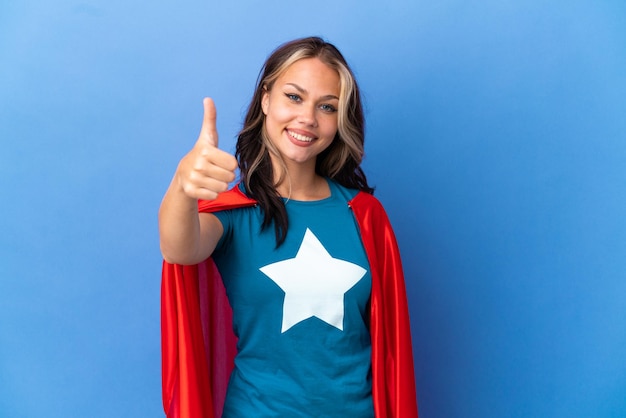 Super Hero Teenager girl isolated on blue background with thumbs up because something good has happened