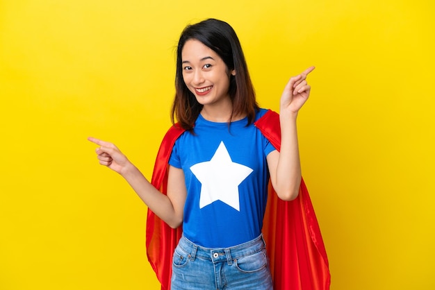 Super hero Vietnamese woman isolated on yellow background pointing finger to the laterals and happy