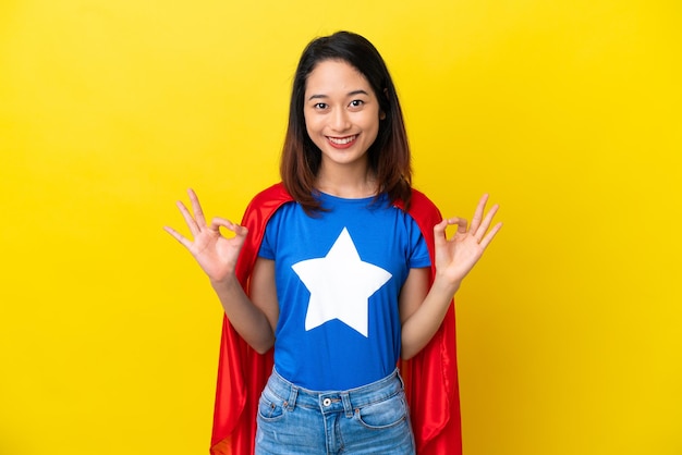 Super hero Vietnamese woman isolated  on yellow background showing an ok sign with fingers