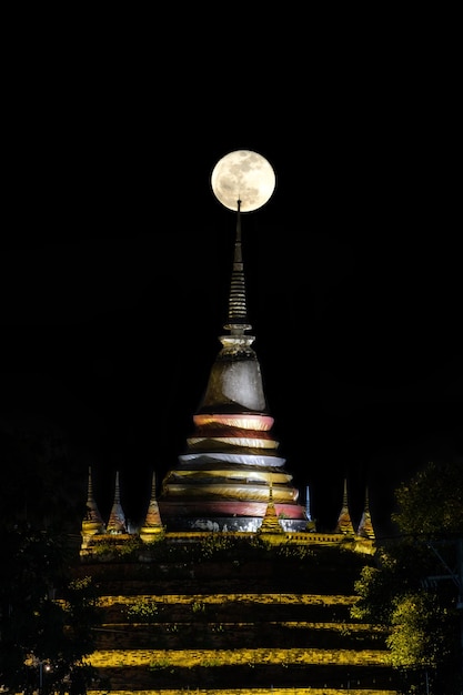 Super moon in night sky and silhouette of ancient pagoda is named Wat Ratchaburana