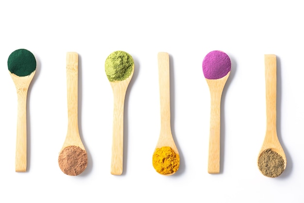 Superfood powders in wooden spoons sweet potato matcha spirulina hemp turmeric carob on a white background Horizontal orientation top view