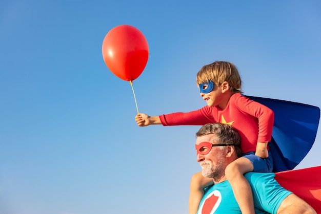 Superhero senior man and child playing outdoor Super hero grandfather and boy having fun together against blue summer sky background Family holiday concept Happy Fathers day