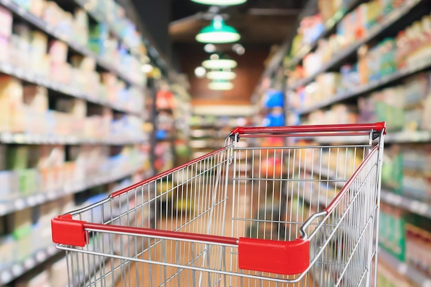 Supermarket aisle blur abstract background with empty red shopping cart