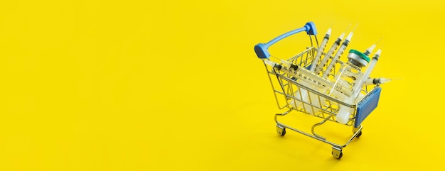 Supermarket trolley with syringes and ampoule on yellow panorama background