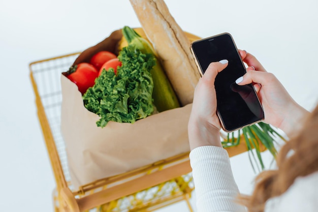 At the Supermarket Woman Uses Smartphone, Leans on the Shopping Cart.