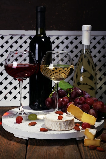 Supper consisting of Camembert cheese wine and grapes on stand on wooden table on white fence background