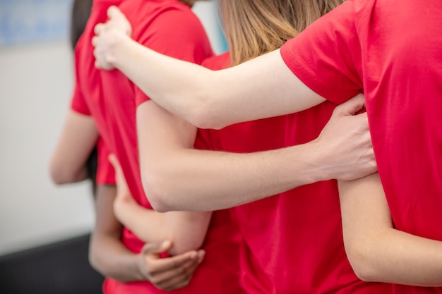 Support, union. Friendly hands hugging the backs of volunteers in red tshirt, faces are not visible